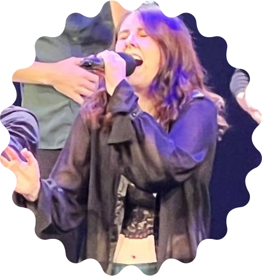 A photo of Anna wearing black and green and singing into a microphone on stage